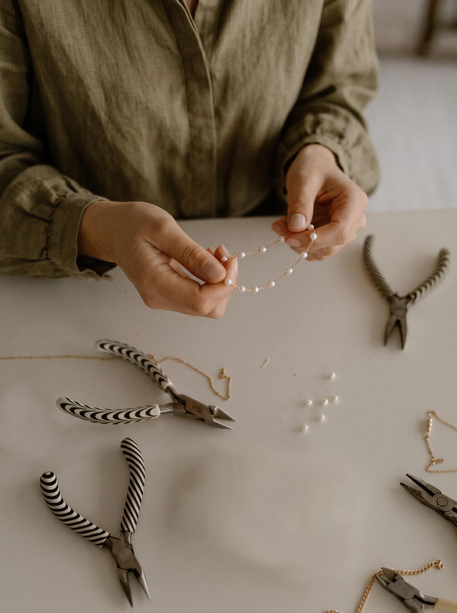 Jewellery maker holding a delicate pearl necklace at her workbench